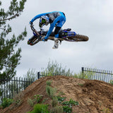 Blue and black motocross gloves gripping handlebars, with printed logos and wrist cuff