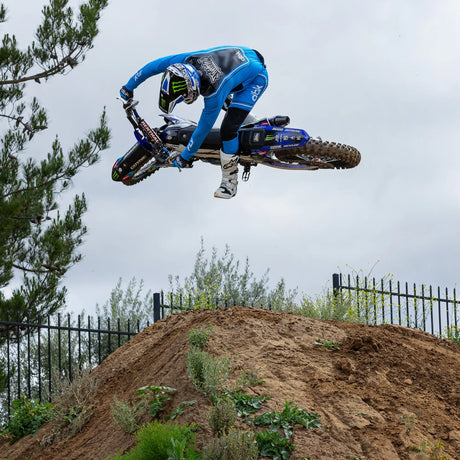 Blue and black motocross gloves gripping handlebars, with printed logos and wrist cuff