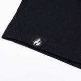 Black T-shirt hem with small flame patch label stitched at the edge