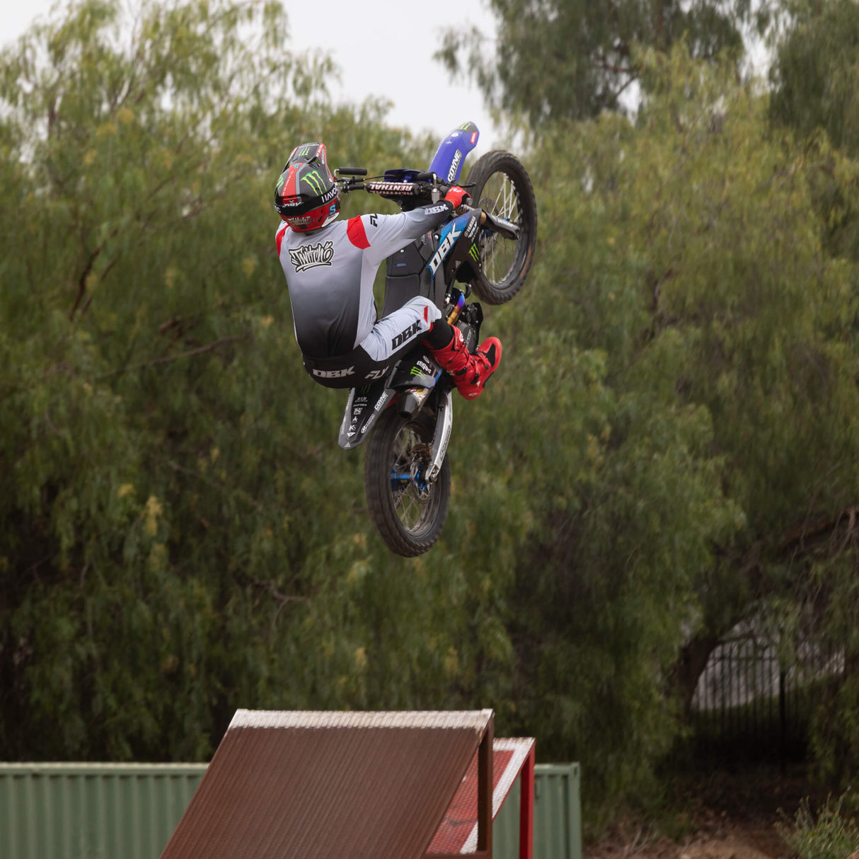 Motorcycle riding pant in white-gray with black panels and red accents, seen during jump