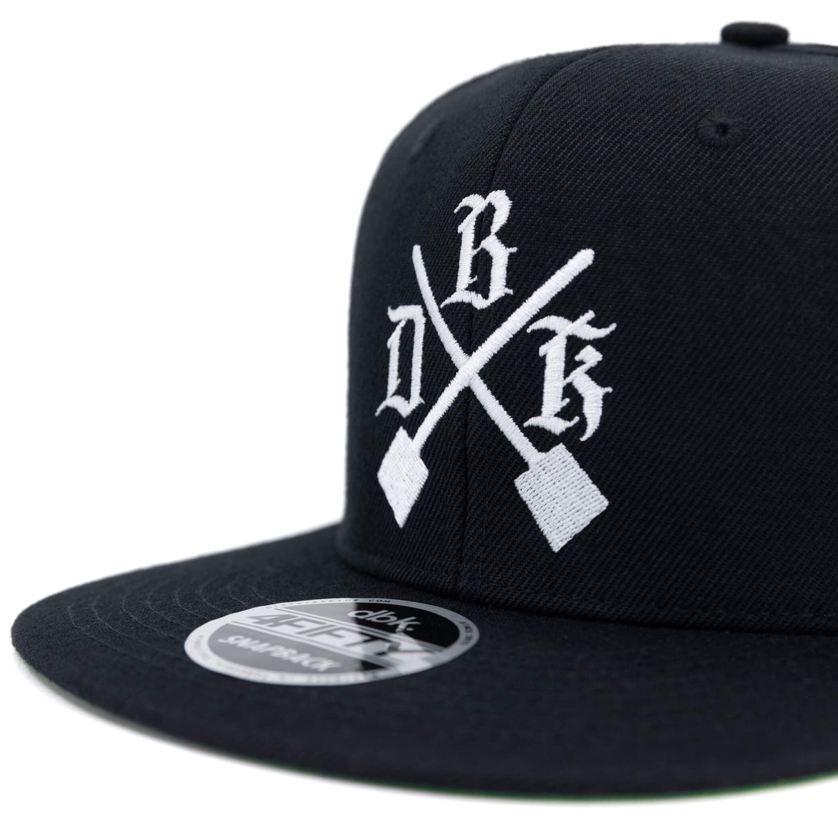 Black snapback cap front close-up with white crossed logo and crown emblem.