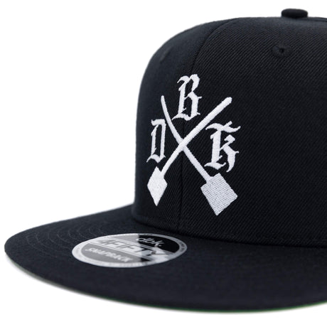 Black snapback cap front close-up with white crossed logo and crown emblem.