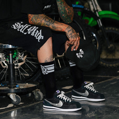 Crew socks worn with sneakers: black sock with white cuff stripes and logo graphic.