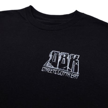 Nahaufnahme: schwarzes T-Shirt mit weißem Brustlogo und Schriftzug „STREETS GOTTA EAT“