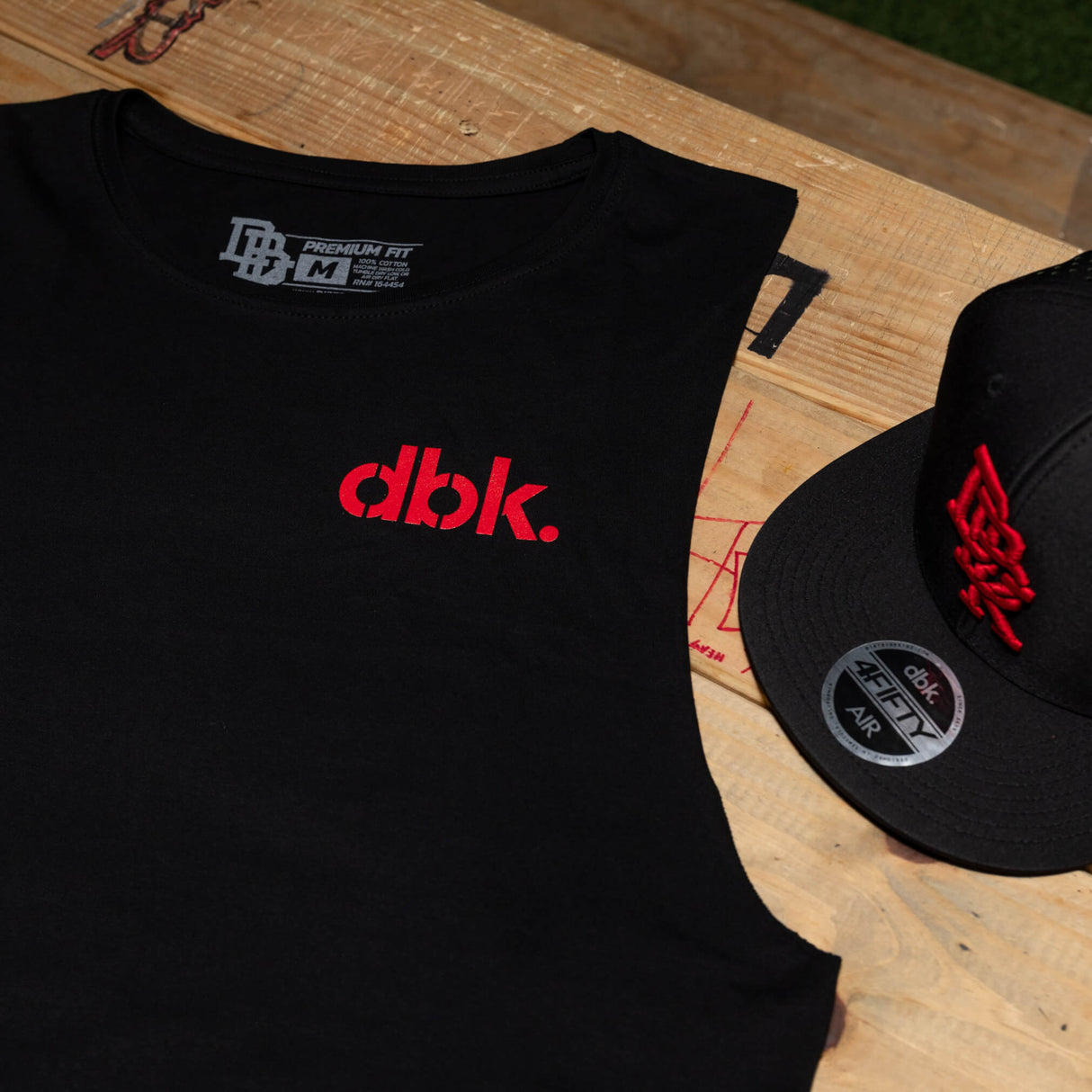 Black tank top with red dbk. logo and neckline label, plus nearby black cap