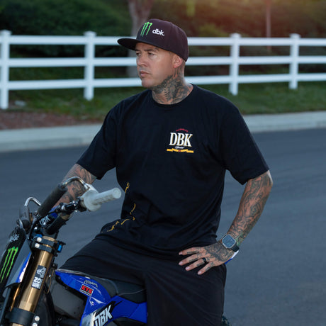 Black graphic T-shirt worn outdoors with DBK logo on the chest