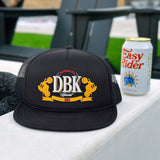 Black trucker hat on white surface, DBK logo patch on front and curved brim