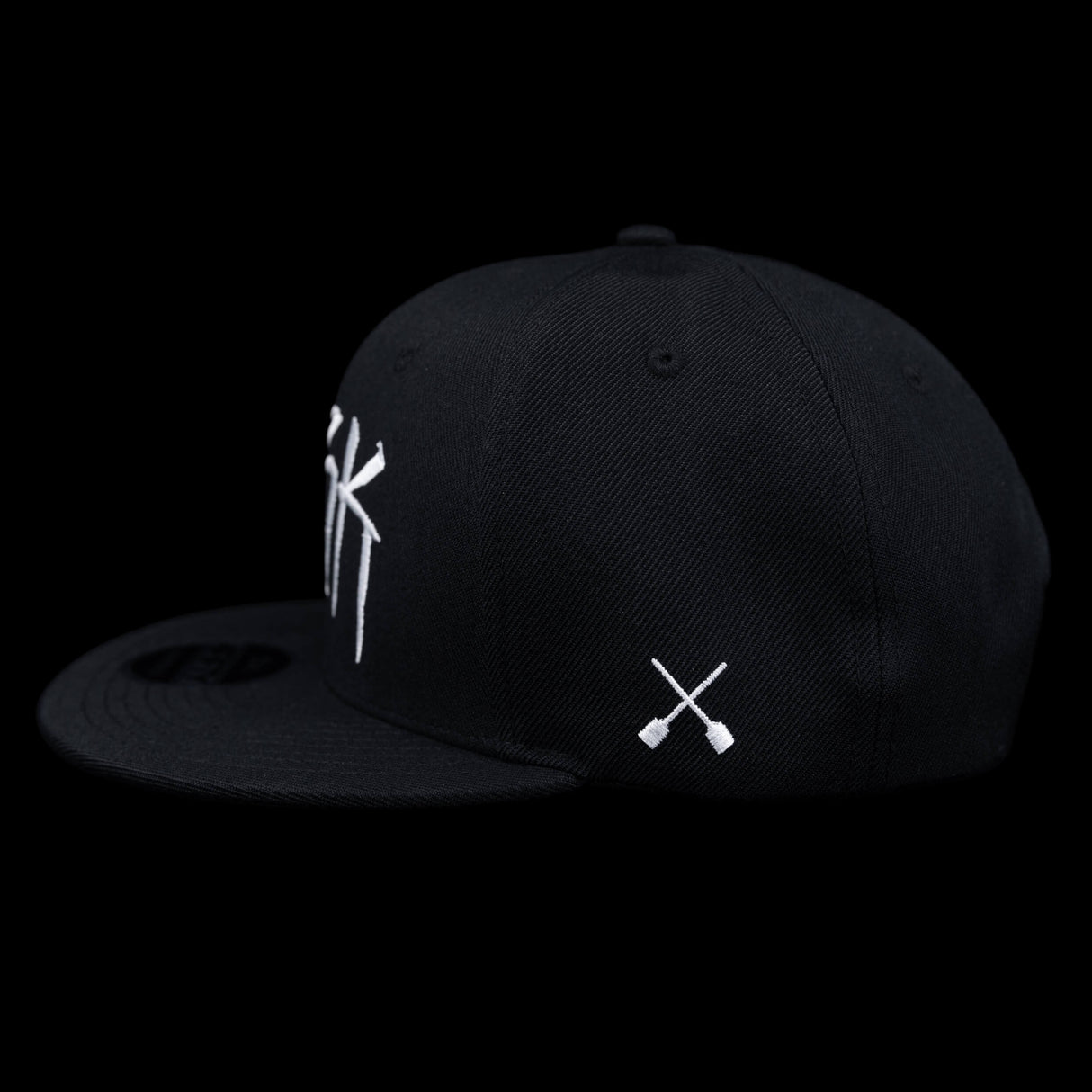 Black snapback cap side view with white X patch on the lower front