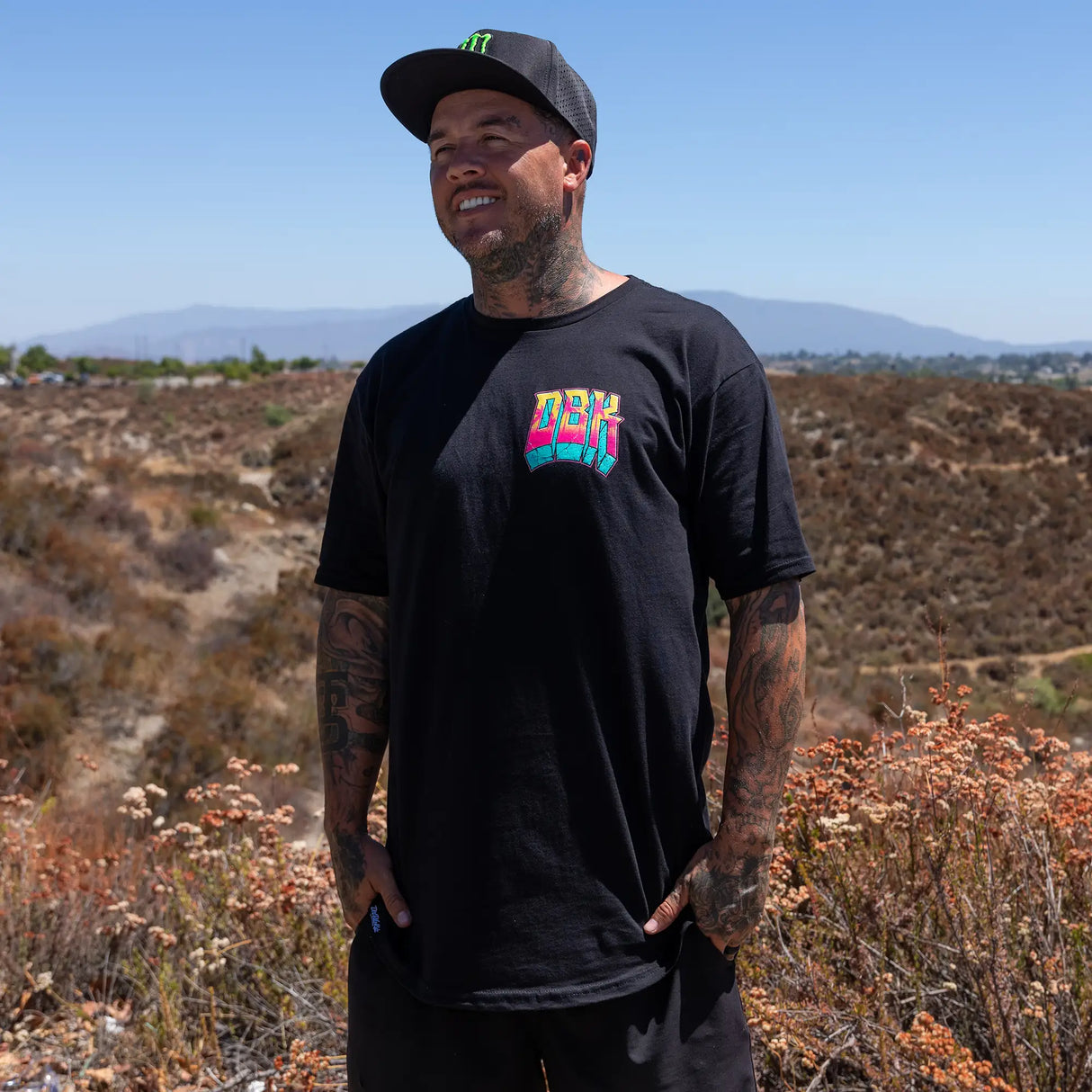 Black crewneck tee with small multicolor DBK front logo worn by person