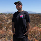 Black crewneck tee with small multicolor DBK front logo worn by person