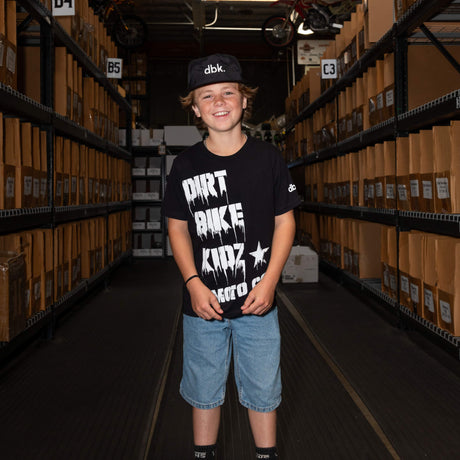 Youth premium tee on model: black shirt with large white "DIRT BIKE KIDZ" artwork