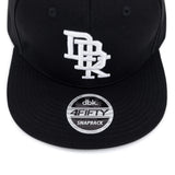 Black snapback cap front with white logo and circular dbk. 4FIFTY SNAPBACK patch