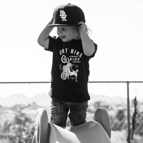 Black toddler T-shirt with front bike rider graphic, child wearing a dark cap
