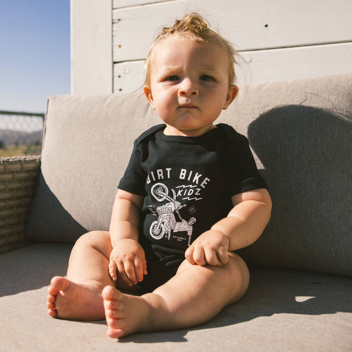 Black baby onesie on sitting baby, short sleeves, bike-themed front graphic