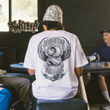 White crew-neck T-shirt with large back print of winged motorcycle emblem.