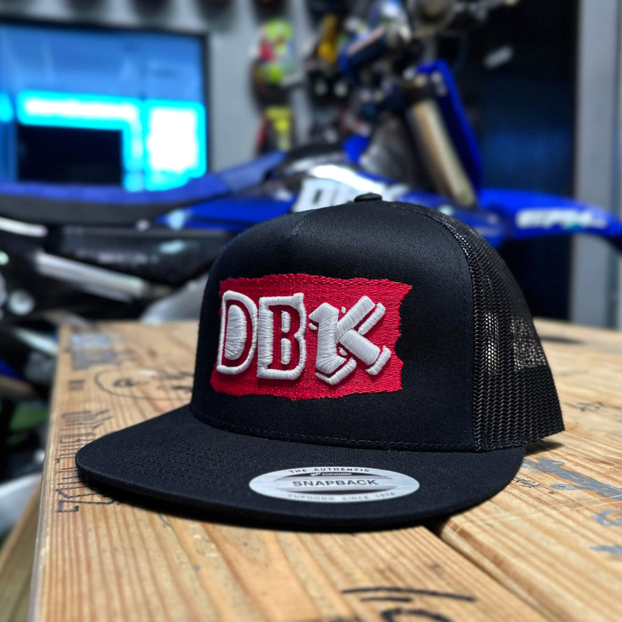 Black trucker hat with DB red logo patch and gray Snapback label on brim