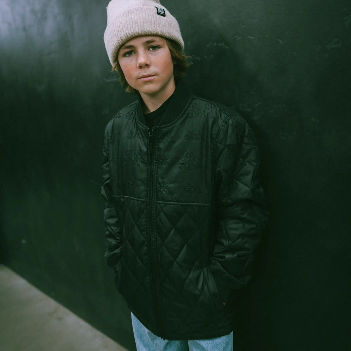 Dark quilted jacket with full zipper and stand collar, worn with beanie