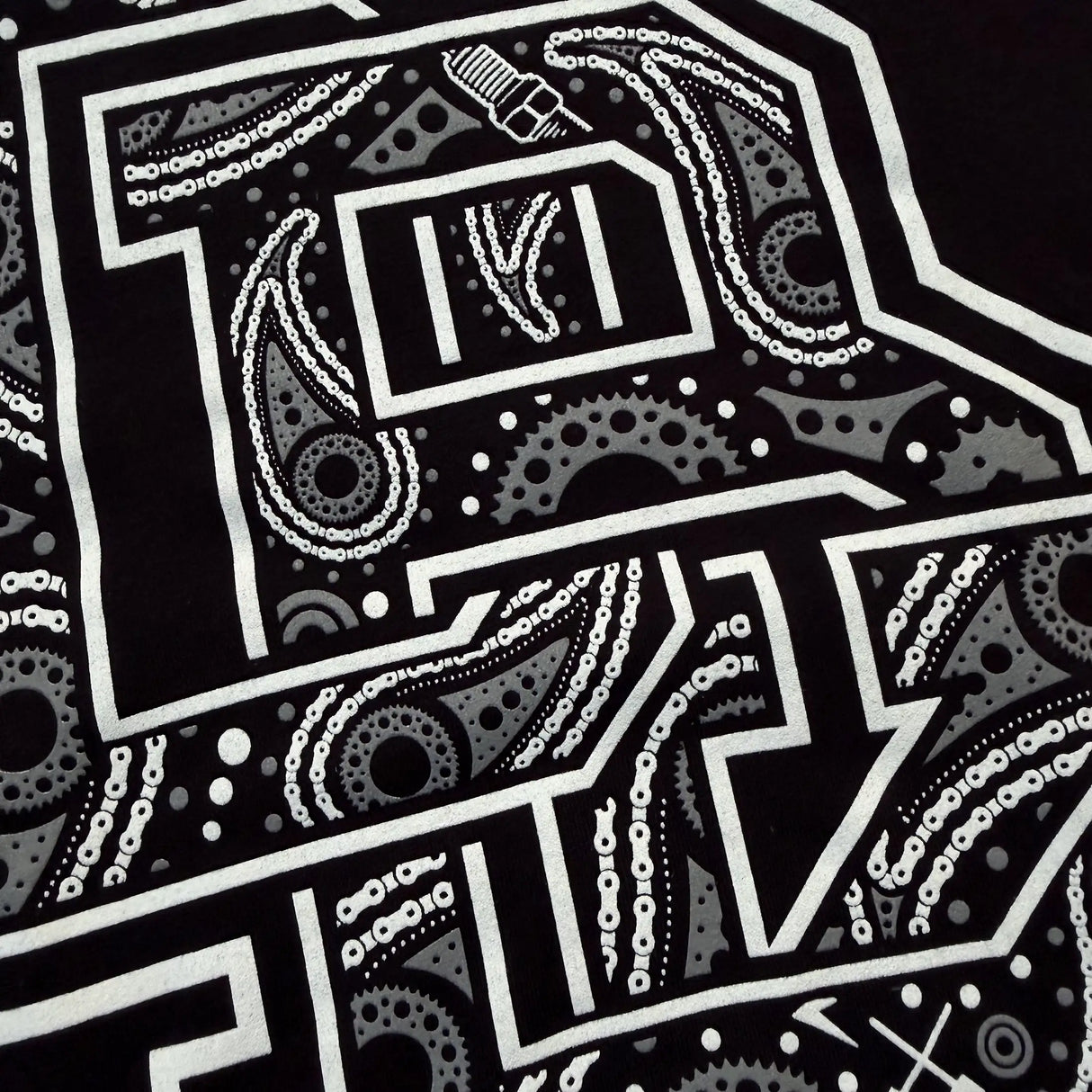 Front graphic close-up on black youth tee: white decorative letter with dots and lines
