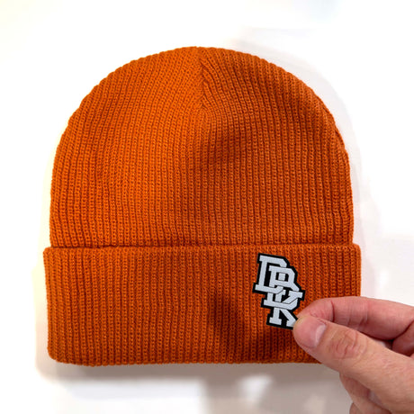 Rust orange ribbed knit beanie with stitched logo patch on cuff