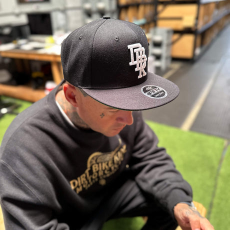 Black snapback cap with white front embroidery and green underside brim
