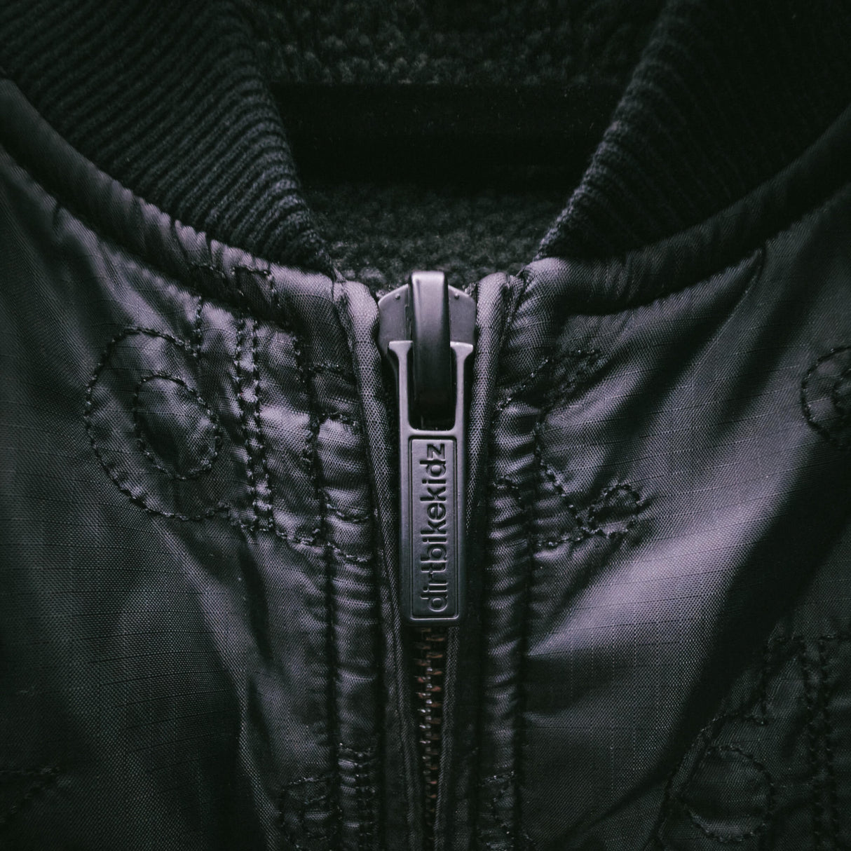 Black jacket zipper with branded pull tab and diamond quilted texture