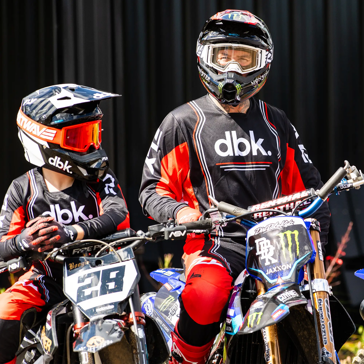 Black and red motocross jersey with gray sleeves, dbk chest logo, worn by riders