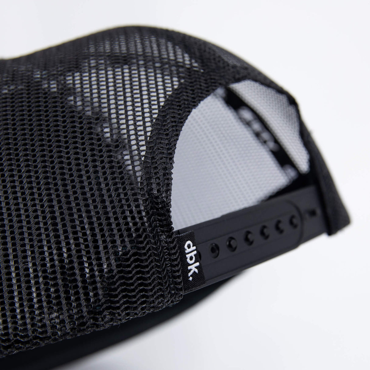 Close-up of black mesh side panel on a trucker cap with small brand label.