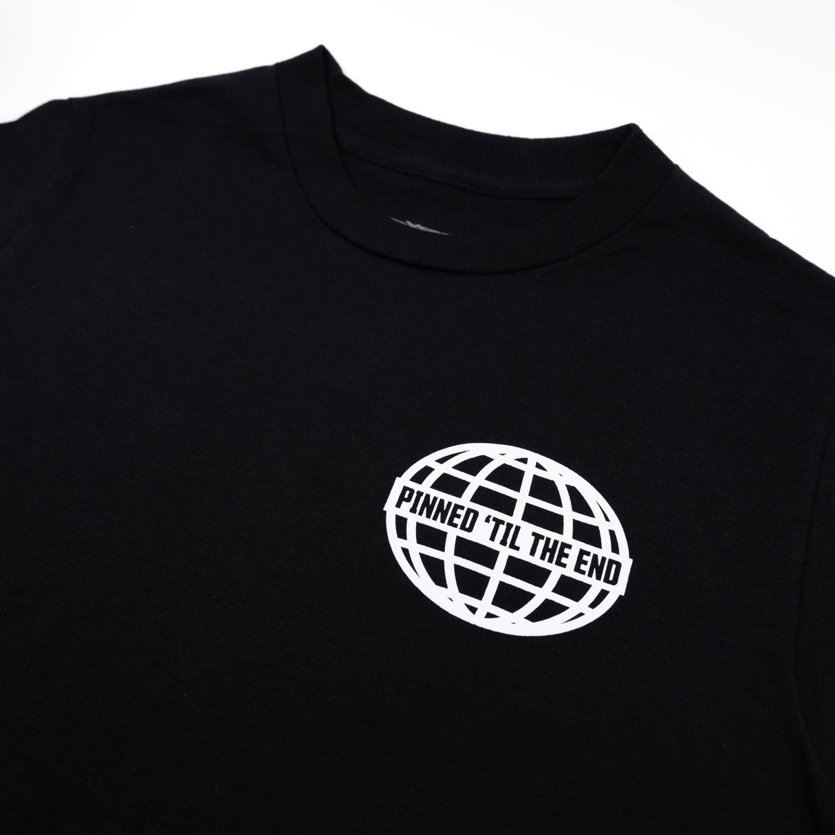 Black T-shirt close-up of white globe logo reading “Pinned Til The End”