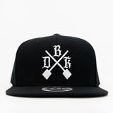 Black snapback with white cross-design graphic and flat brim