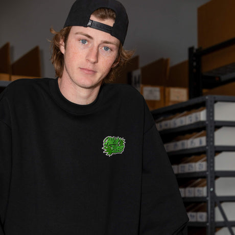 Schwarzes Crewneck-Sweatshirt mit grünem Brustlogo am Modell, lange Ärmel