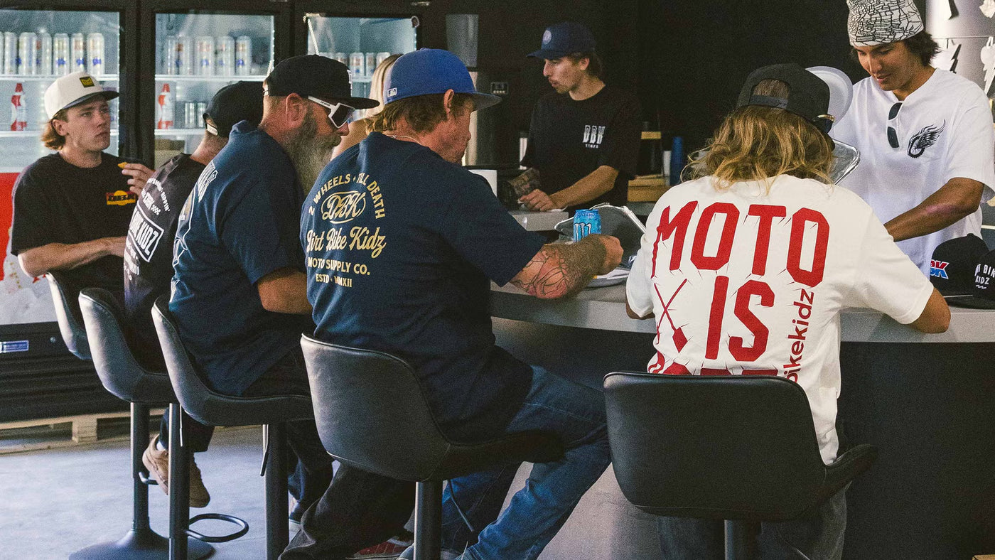 Group of DBK athletes sitting around a table in a casual setting, with one person wearing a 'Moto Is Dope' shirt.