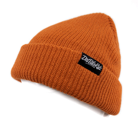 Rust orange beanie, angled view with black logo patch on the cuff