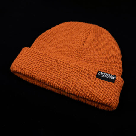 Rust orange cuffed beanie, side view with black logo label