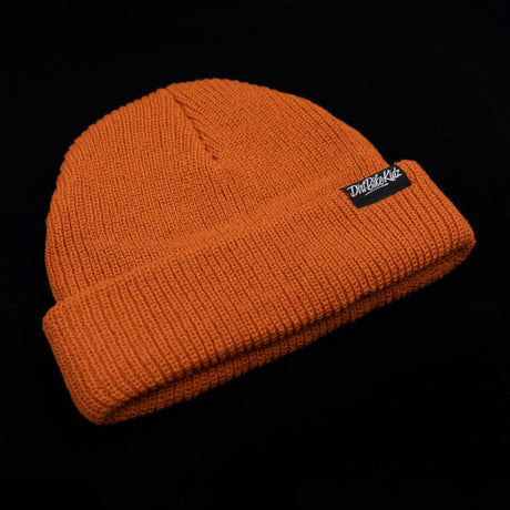 Rust orange knitted beanie with slouchy crown and black logo patch