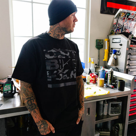 Black T-shirt worn by man, side view; large camo-style front graphic.