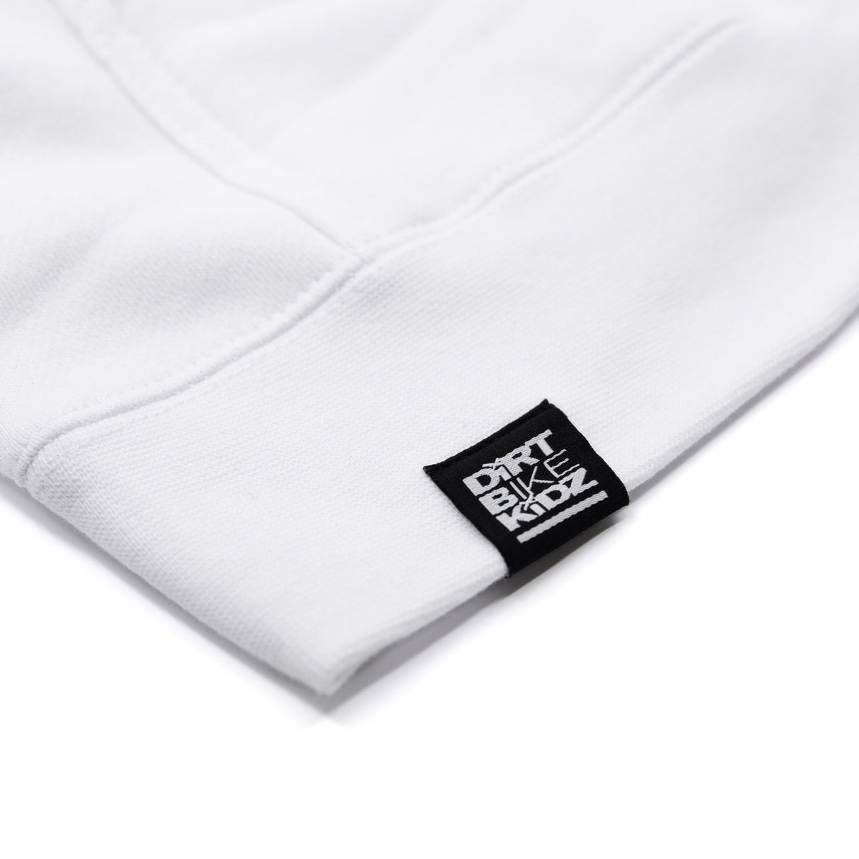 White hoodie cuff close-up with small woven brand label on sleeve hem.