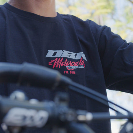 Close-up of black Factory Tee back graphic: DBK with red Motorcycle text.