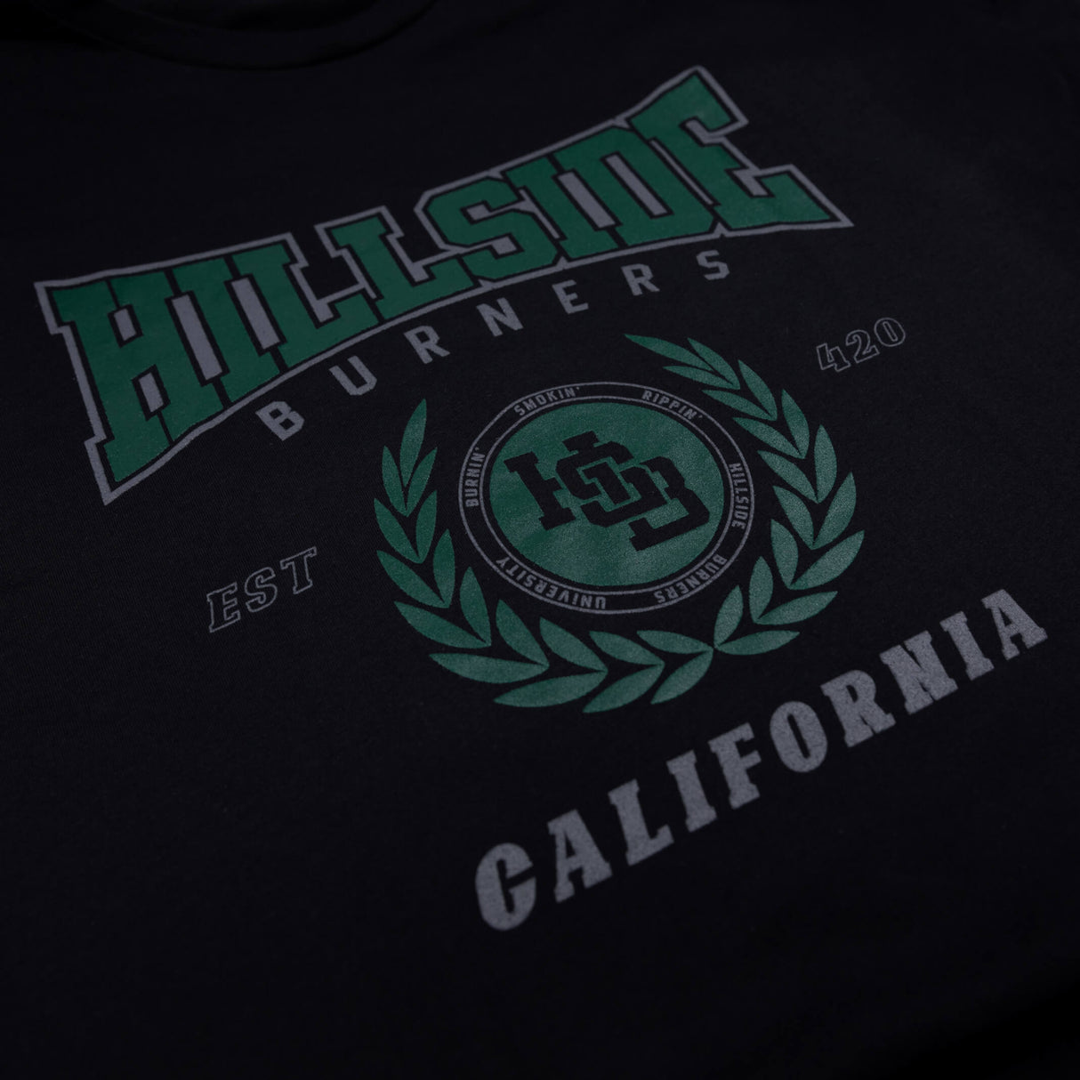 Black varsity tee close-up of green “Hillside” front logo and crest