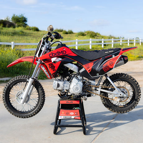 Honda CRF 110 dirt bike in red and black with graphics, front view on stand