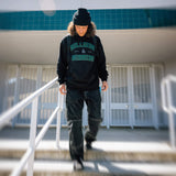 Black varsity hoodie with green logo print and hood, worn with beanie