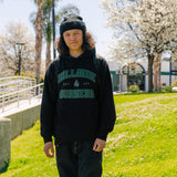 Varsity hoodie on model: black pullover with hood and green logo graphic