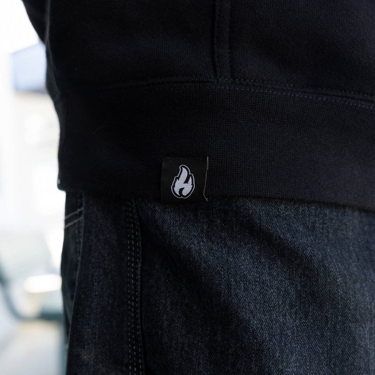 Black hoodie fabric close-up with white flame logo patch near side seam