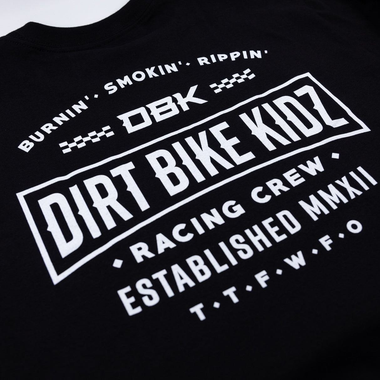 Black crewneck T-shirt close-up of DBK Dirt Bike Kidz racing crew and established logo.