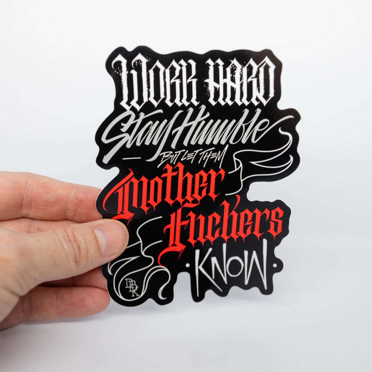 Die-cut typographic sticker with red, white, and black lettering, held in hand
