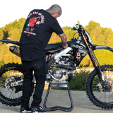 Black T-shirt with back graphic and red text worn by man beside dirt bike