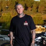Black T-shirt with small red DBK flame logo on left chest worn by man