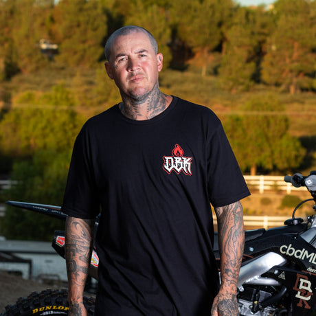 Black T-shirt with small red DBK flame logo on left chest worn by man